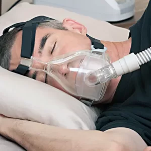 a man lying on his side on a pillow in bed with a full mask CPAP machine to help him breathe